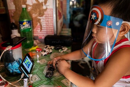 Một bé trai đội mũ ngăn giọt bắn ngồi học trực tuyến qua điện thoại tại Manila, Philippines. Ảnh: Reuters